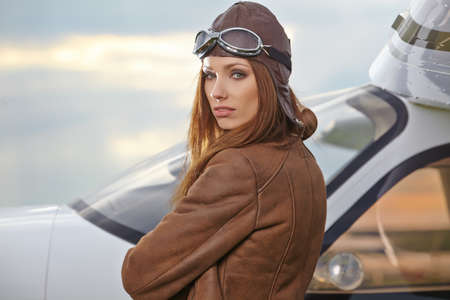 A young female pilot is standing next to a small training planeの写真素材