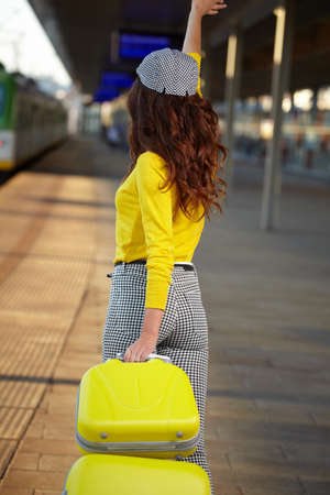 A woman with yellow travel suitcases is waiting for a train at the train stationの写真素材