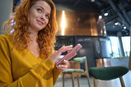 Portrait of smiling young woman sitting in cafe at center mall and using smartphone.の写真素材