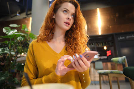 Portrait of smiling young woman sitting in cafe at center mall and using smartphone.の写真素材