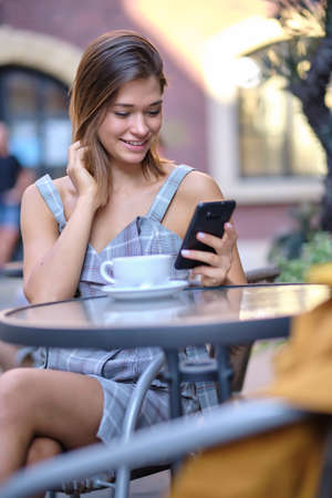 A woman is sitting in a cafe on the street and talking on the phoneの写真素材