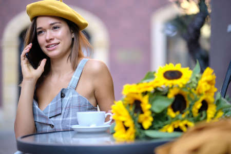 A woman is sitting in a cafe on the street and talking on the phoneの写真素材