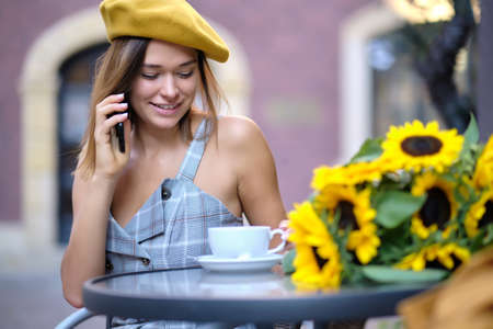 A woman is sitting in a cafe on the street and talking on the phoneの写真素材