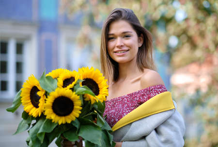 Street portrait of a beautiful young woman holding a sunflowerの写真素材
