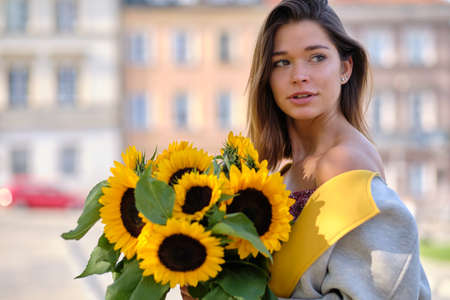Street portrait of a beautiful young woman holding a sunflowerの写真素材