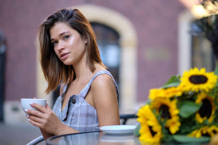 young stylish woman sitting in cafe, holding drinking cup cappuccinoの写真素材