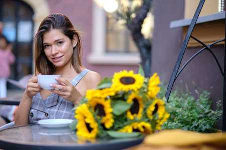 young stylish woman sitting in cafe, holding drinking cup cappuccinoの写真素材
