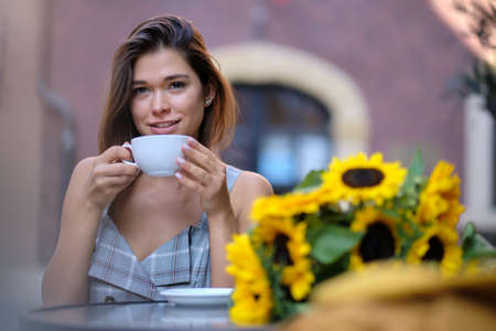 young stylish woman sitting in cafe, holding drinking cup cappuccinoの写真素材