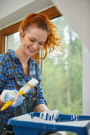 Smiling young woman painting walls in her new house: home renovation and DIY conceptの写真素材