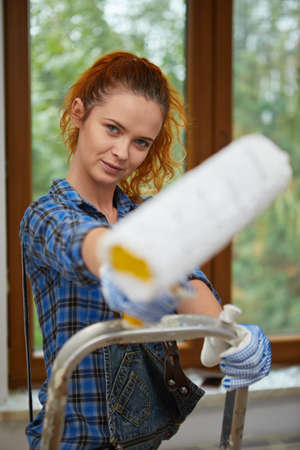 Happy smiling woman doing renovation and painting walls with paint rollerの写真素材