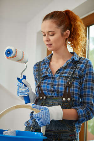 Happy smiling woman doing renovation and painting walls with paint rollerの写真素材