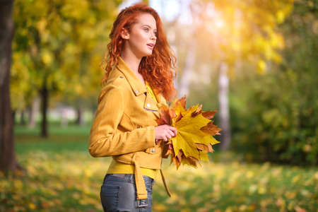 Cute redhaired woman holding autumn leafs in the nature.の写真素材
