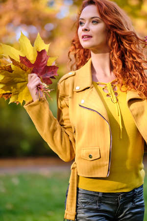 Cute redhaired woman holding autumn leafs in the nature.の写真素材