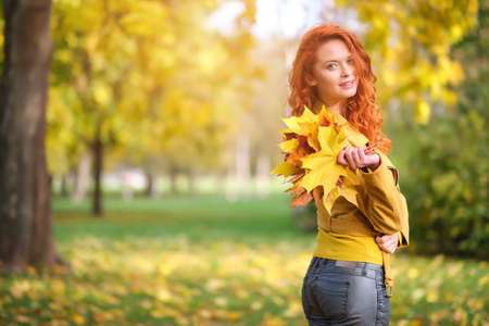 Cute redhaired woman holding autumn leafs in the nature.の写真素材
