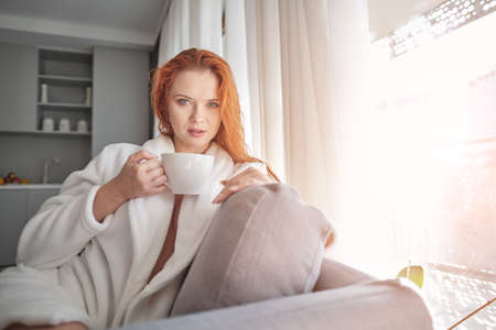 Beautiful young woman with cup of coffee at homeの写真素材