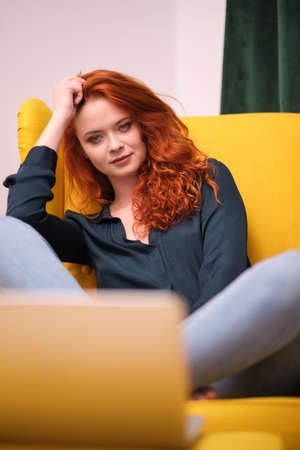 Nice beautiful lady with redhead curly hair work at the notebook sit down on the sofa at home - check on oline shops for cyber monday sales - technology woman concept for alternative office freelanceの写真素材