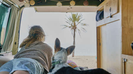 girl and her dog on a bed of a self converted camper van looking through the window living van lifeの写真素材