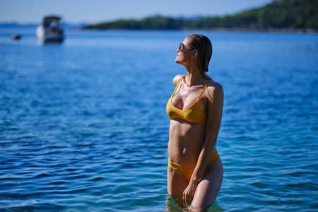 Beautiful woman in striped bikini on beach with copy space. Tanned girl in swimwear enjoying on beach.の写真素材