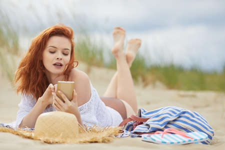 Beautiful young woman uses a smartphone, lyingの写真素材