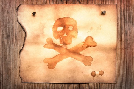 Old paper with jolly roger attached to wooden wallの写真素材