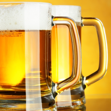 Beer mugs with froth over yellow background の写真素材
