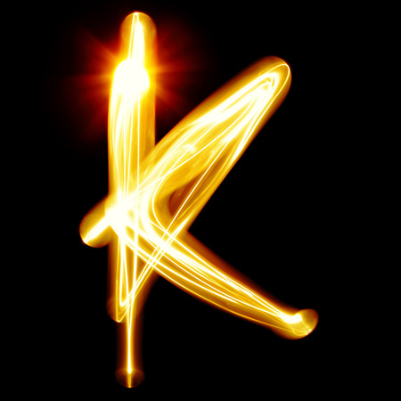 K - Created by light alphabet over black backgroundの写真素材
