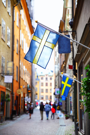 Perspective of old street in Stockholm with swedish flags, Sweden. Shallow DOF, focus on the first flagのeditorial素材