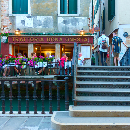 Venice, Italy - June 18, 2018: People at small restaurant with tables outdoors near small canal in Veniceのeditorial素材