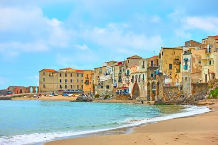 Sandy beach and old houses by the sea in Cefalu, Sicily, Italyの写真素材