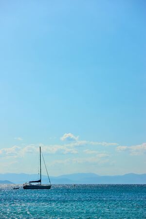 Single sail yacht in the sea near islands and blue sky with clouds. Vertical seascape with large space for your own textの写真素材