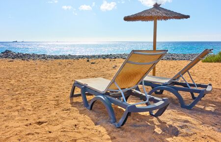 Sandy beach with parasol and chaise longues by the sea on sunny summer day