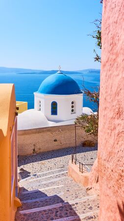Street and Greek orthodox church with blue dome by the sea in Oia town in Santorini island, Greeceの写真素材