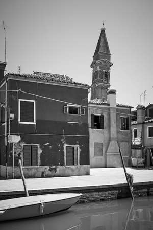 Waterfront by canal and leaning old bell tower in Burano in Venice, Italy  - Black and white photography, italian cityscapeの写真素材