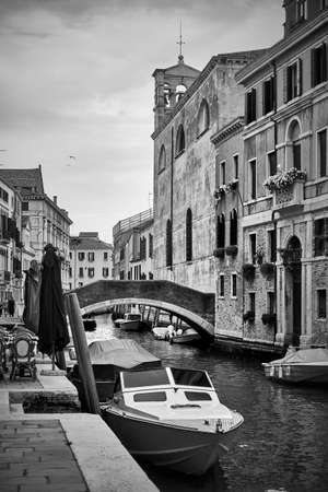 Venetian canal with bridge and moored motorboats, Venice, Italy. Black and white photography, cityscapeの写真素材