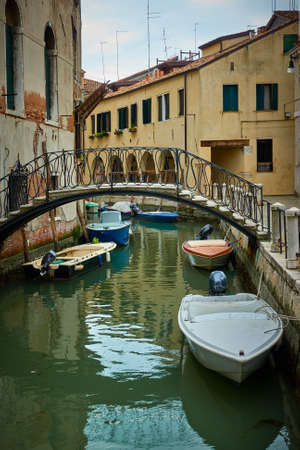 Venetian canal with bridge and moored motorboats, Venice, Italy.の写真素材