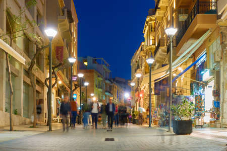 Heraklion, Crete, Greece - April 26, 2018: 25th August street in Heraklion city at night with walking people. People are blurred in motionのeditorial素材