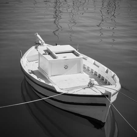 Small white fishing boat in the harbour. Black and white photography