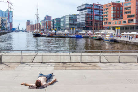 Hamburg, Germany - August 18, 2012:  Young man sunbuths by the water on stairs at Sandtorkai...