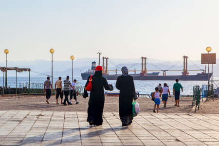 Aqaba, Jordan - May 23, 2009: Walking people at waterfront in Aqaba city and cargo ships in the gulf