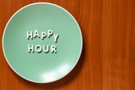 Happy Hour - Plate with text on wooden table and space for your own textの写真素材