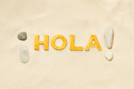 Hola! - Spanish greeting by golden letters in the white sandの写真素材