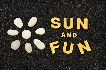 Sun And Fun - Text in black beach sand with Sun symbol by sea pebblesの写真素材