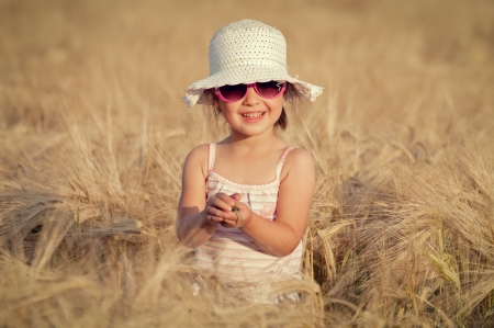 Cute happy girl walking in the field of wheat on sunny spring dayの写真素材