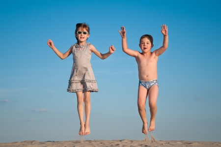 happy siblings jumping over sandの写真素材