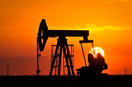 An oil pump jack is silhouetted by the setting sunの写真素材