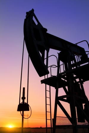 An oil pump jack is silhouetted by the setting sunの写真素材