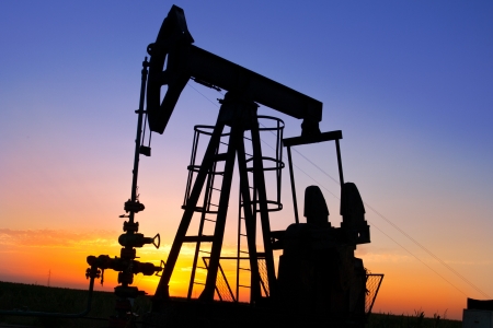 An oil pump jack is silhouetted by the setting sunの写真素材