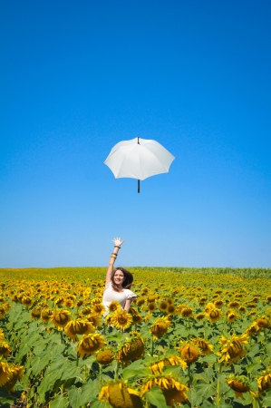 Young woman with umbrella on field in sunflowerの写真素材