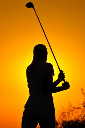 woman golf player tee off during sunset silhouettedの写真素材