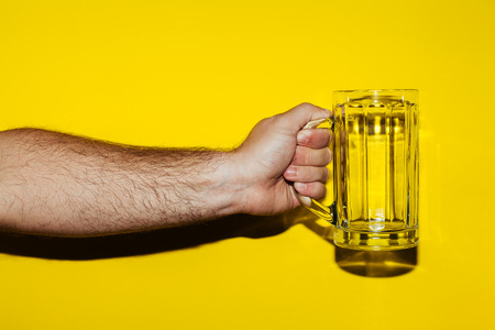 Hand hold mug of beer on yellow backgroundの写真素材